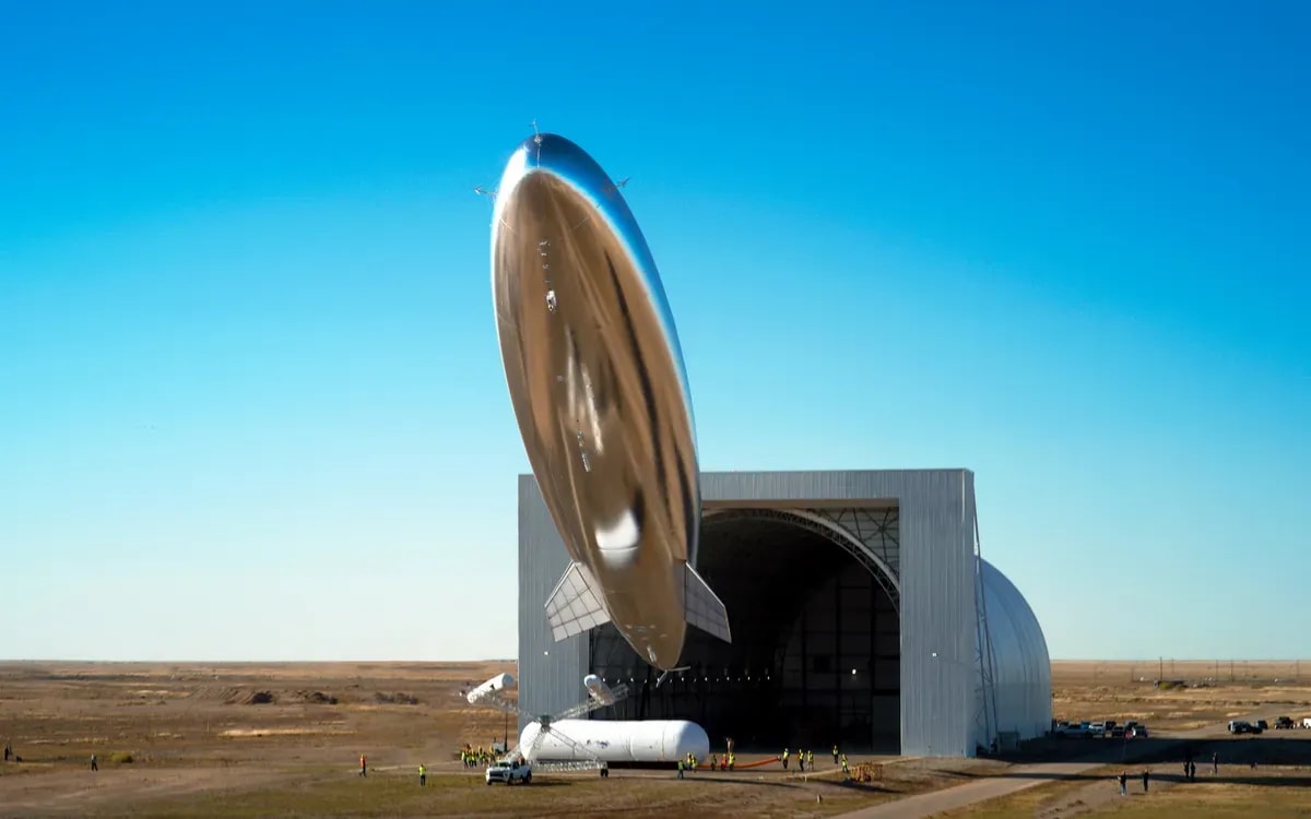 desert-scene-with-silvery-airship-floating-into-sky-launched-from-an-aircraft-hangar.webp